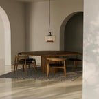 Small amber Clérachic pendant over a large round wooden table in an arched room with a speckled rug.