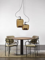 Two amber glass Clérachic pendants hang above a round table with four green chairs on a woven rug.