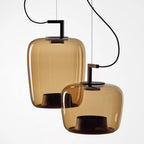 Close view of two amber glass Clérachic pendants, a tall one behind a squat one, with their black bases visible.