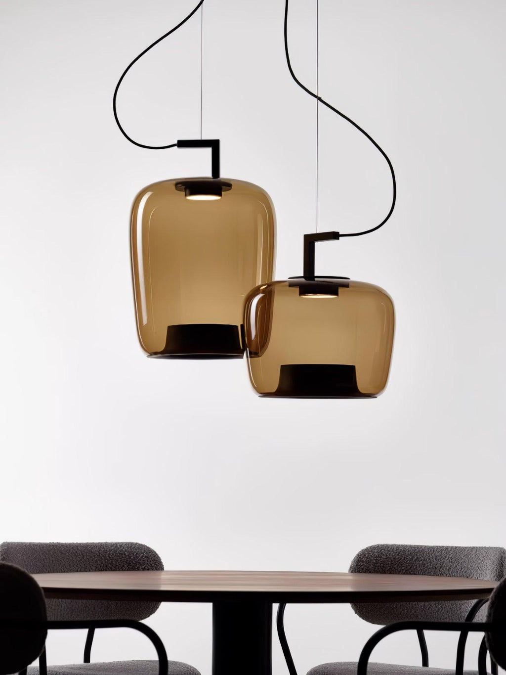 Two amber glass Clérachic pendants hang above a dark round table and chairs, cropped at the bottom of the frame.