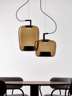 Two amber glass Clérachic pendants hang above a dark round table and chairs, cropped at the bottom of the frame.
