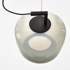 Close view from below of a foggy white glass Clérachic pendant, its black disc cap and a glowing opening visible.