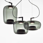Three smoke grey glass Clérachic pendants in tall, squat and wide shapes, hanging together on a white backdrop.