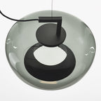 Close view from below of a rounded grey glass Clérachic pendant, with its black disc cap and a dark ring opening.