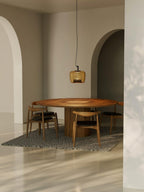 Distant view of an amber Clérachic pendant above a round wooden table in an arched room with a patterned rug.