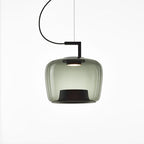 Squat grey-green glass Clérachic pendant with ribbed edges and a black base, lit softly on a white backdrop.