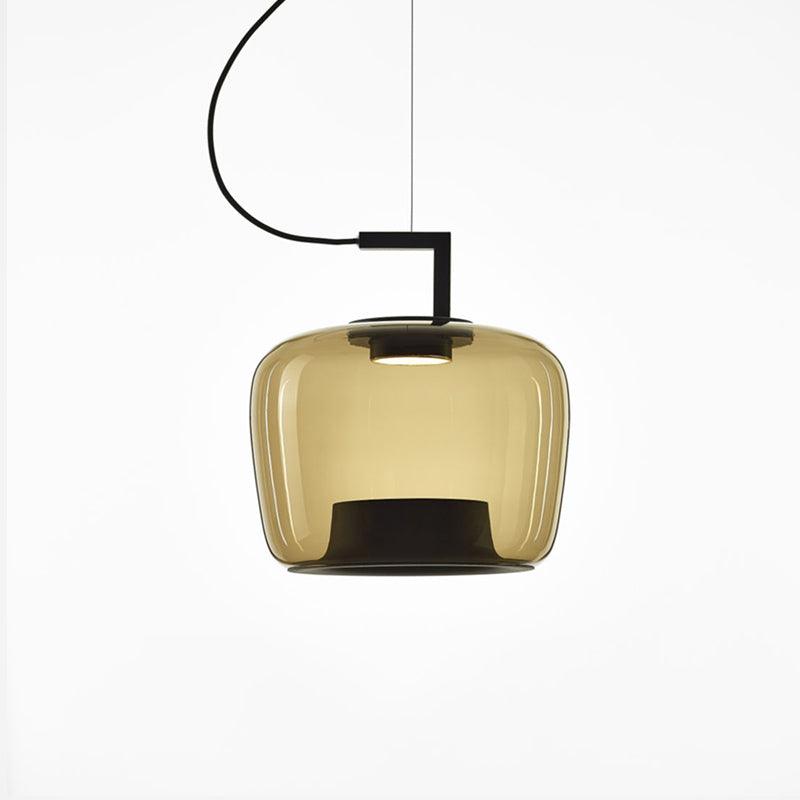 Squat amber glass Clérachic pendant with a black bracket and a black inner base, lit on a white backdrop.