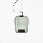 Tall grey-green glass Clérachic pendant with a black bracket and a dark base, lit on a white backdrop.