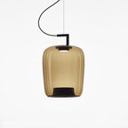 Tall amber glass Clérachic pendant with a black bracket and a dark inner base, lit on a white backdrop.