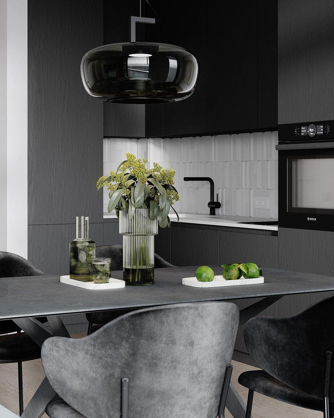 Wide smoke grey glass Clérachic pendant above a dark table set with a vase, glasses and limes, in a black kitchen.
