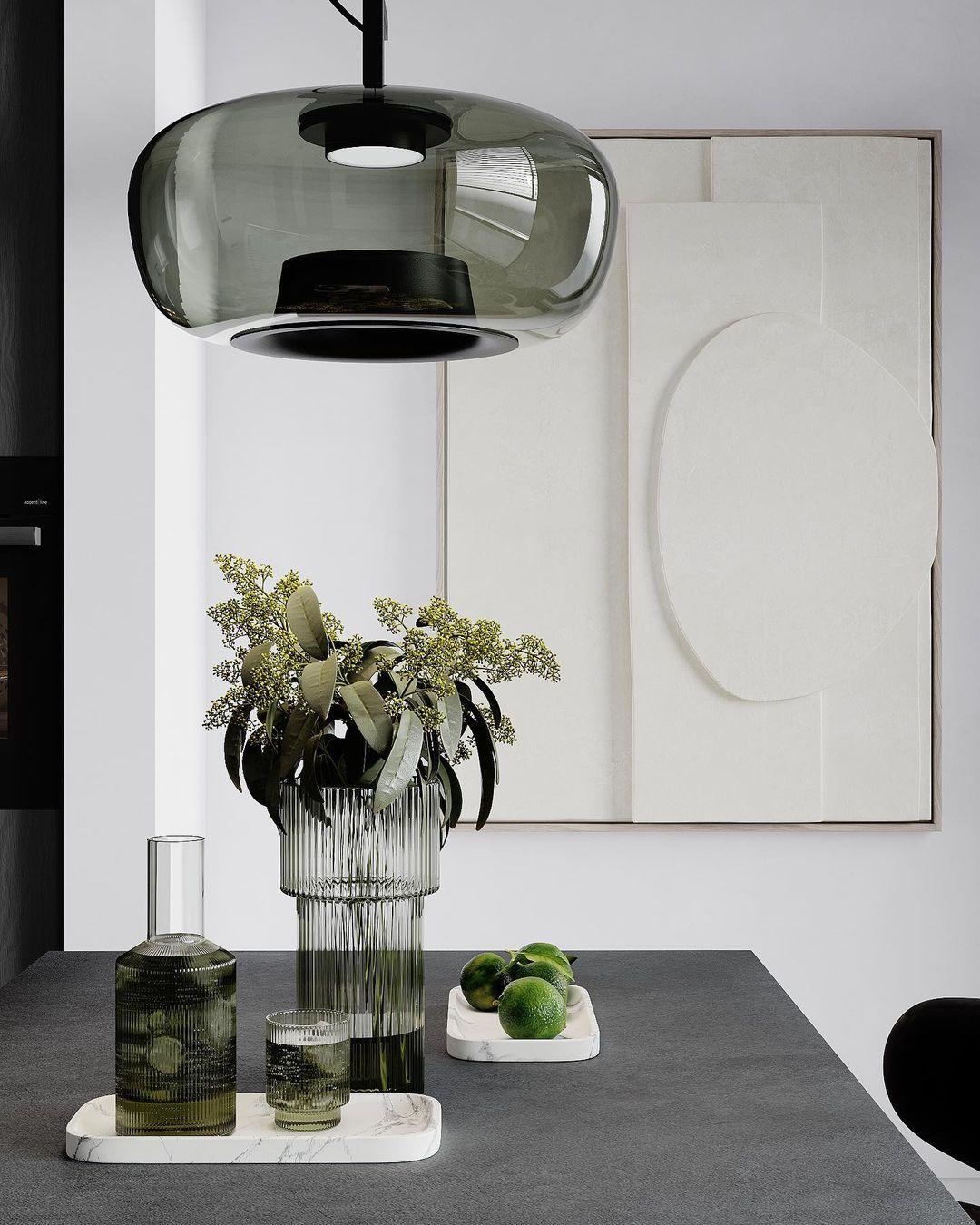 Close view of a smoke grey glass Clérachic pendant above a table with a ribbed vase, a carafe and limes.