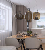 Three amber-brown Clérachic pendants hang above a wooden dining table with grey chairs, beside a curtained window.