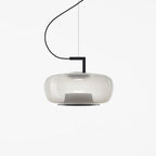 Wide pale grey glass Clérachic pendant with a soft glow and a black bracket on a plain white backdrop.