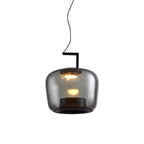 Squat smoke grey glass Clérachic pendant with the bulb glowing warmly inside, on a white backdrop.