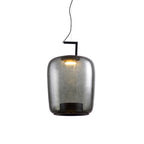 Tall smoke grey glass Clérachic pendant with a warm light glowing at its top, on a white backdrop.