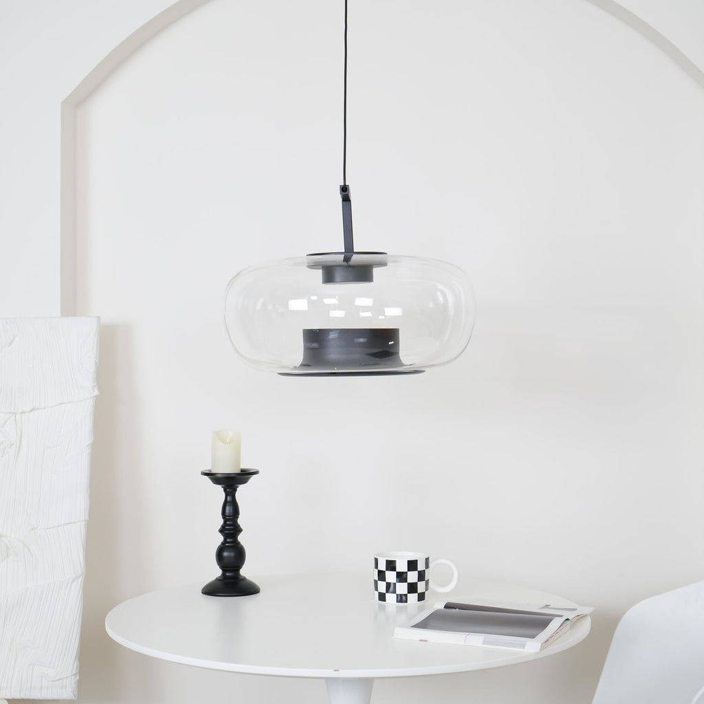 Wide clear glass Clérachic pendant before a white arch, above a round white table with a candlestick and a checked mug.