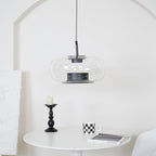 Wide clear glass Clérachic pendant before a white arch, above a round white table with a candlestick and a checked mug.