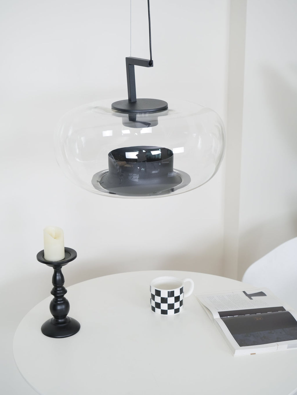 Close view of a wide clear glass Clérachic pendant, showing its black collar and base ring above a candlestick.