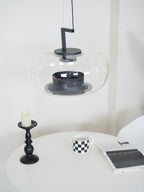 Close view of a wide clear glass Clérachic pendant, showing its black collar and base ring above a candlestick.