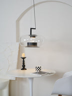 Wide clear glass Clérachic pendant before a plaster arch, above a small tulip table with a candle and a checked mug.