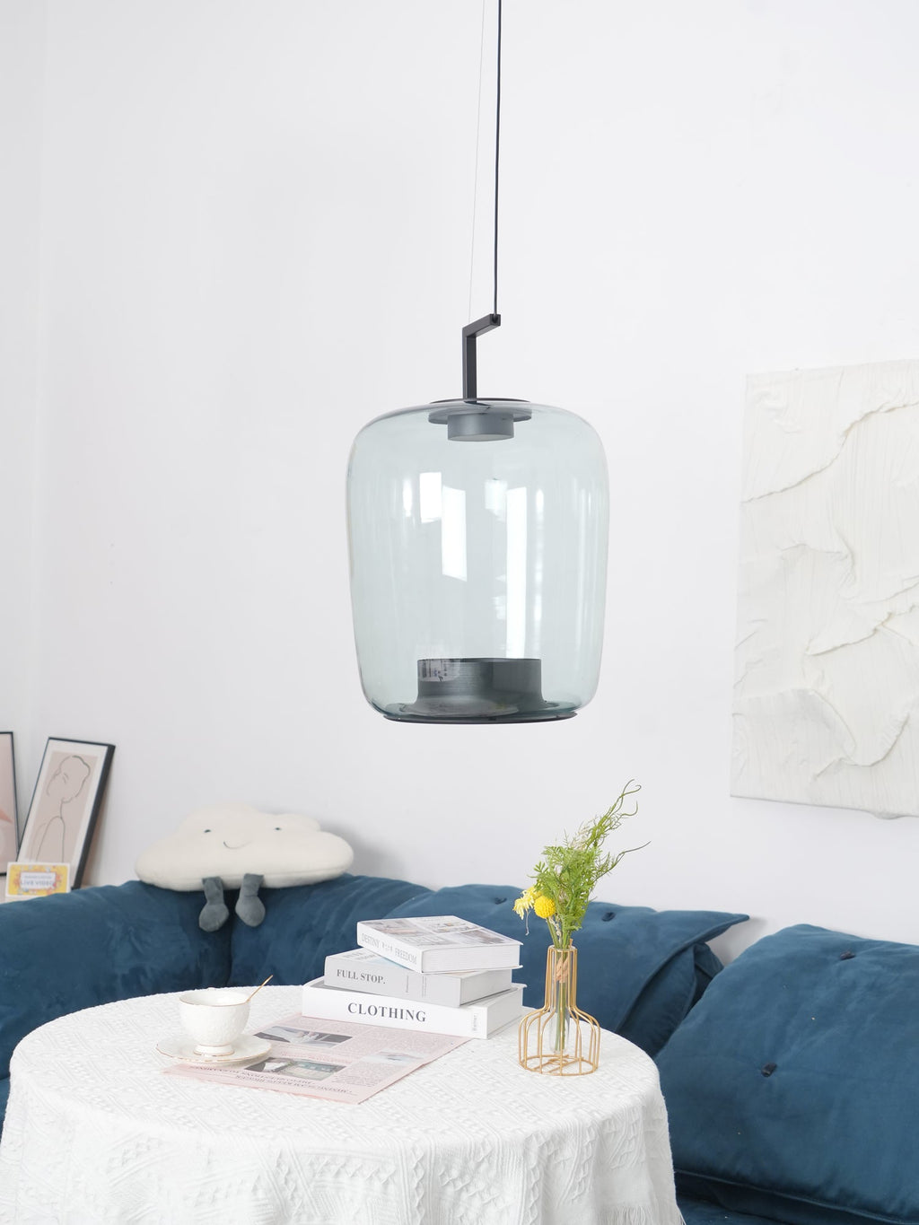 Smaller view of a tall grey-green glass Clérachic pendant above a lace-covered table and a blue sofa.
