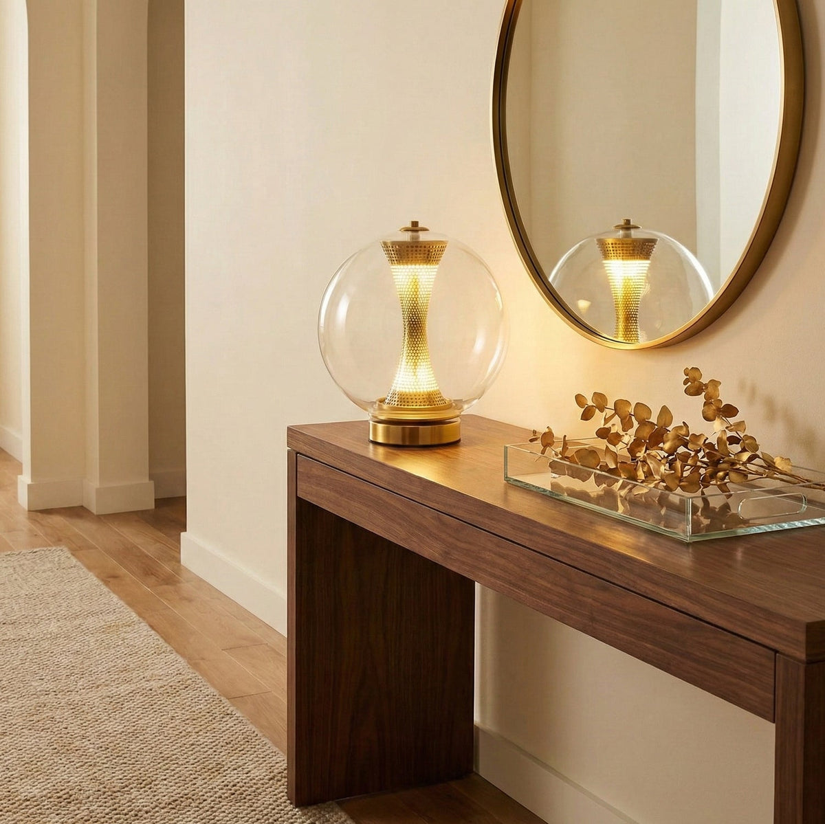 This Clérachic sphere lamp lit on a walnut console table, reflected in an oval brass-framed mirror with dried gold stems nearby.