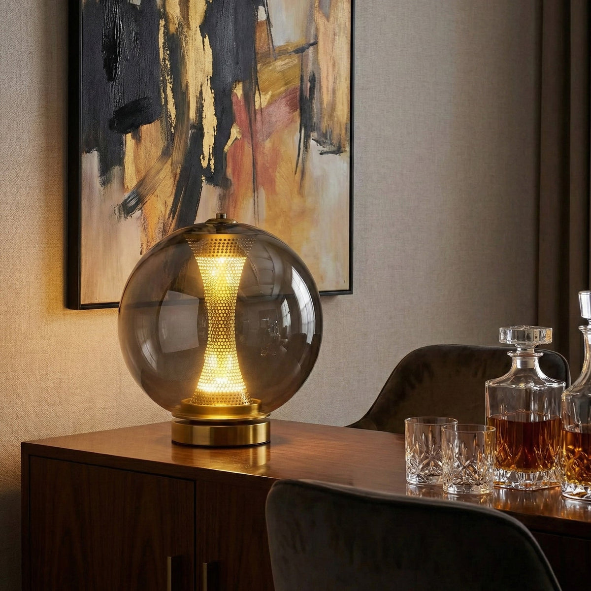 Smoky grey sphere of this Clérachic lamp glowing on a dark sideboard, with whisky glasses, a decanter and a gold-and-black painting.