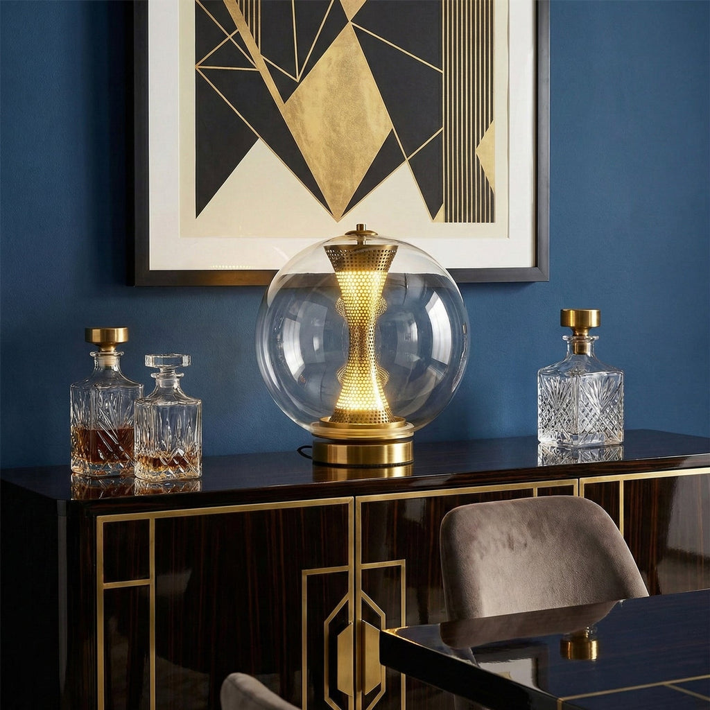 This Clérachic sphere lamp lit on a black and gold cabinet, against a navy wall with a geometric gold artwork and crystal decanters.