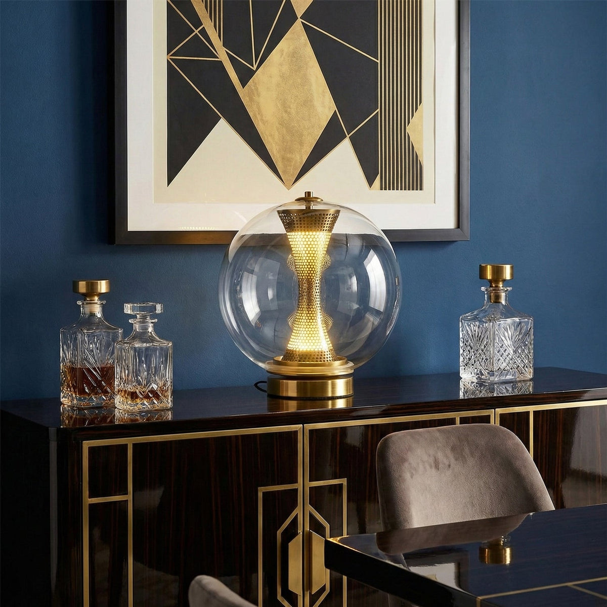 This Clérachic sphere lamp lit on a black and gold cabinet, against a navy wall with a geometric gold artwork and crystal decanters.