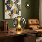 Smoky grey sphere lamp from Clérachic on a walnut desk in a green-walled study, with a tan leather chair and glasses beside it.