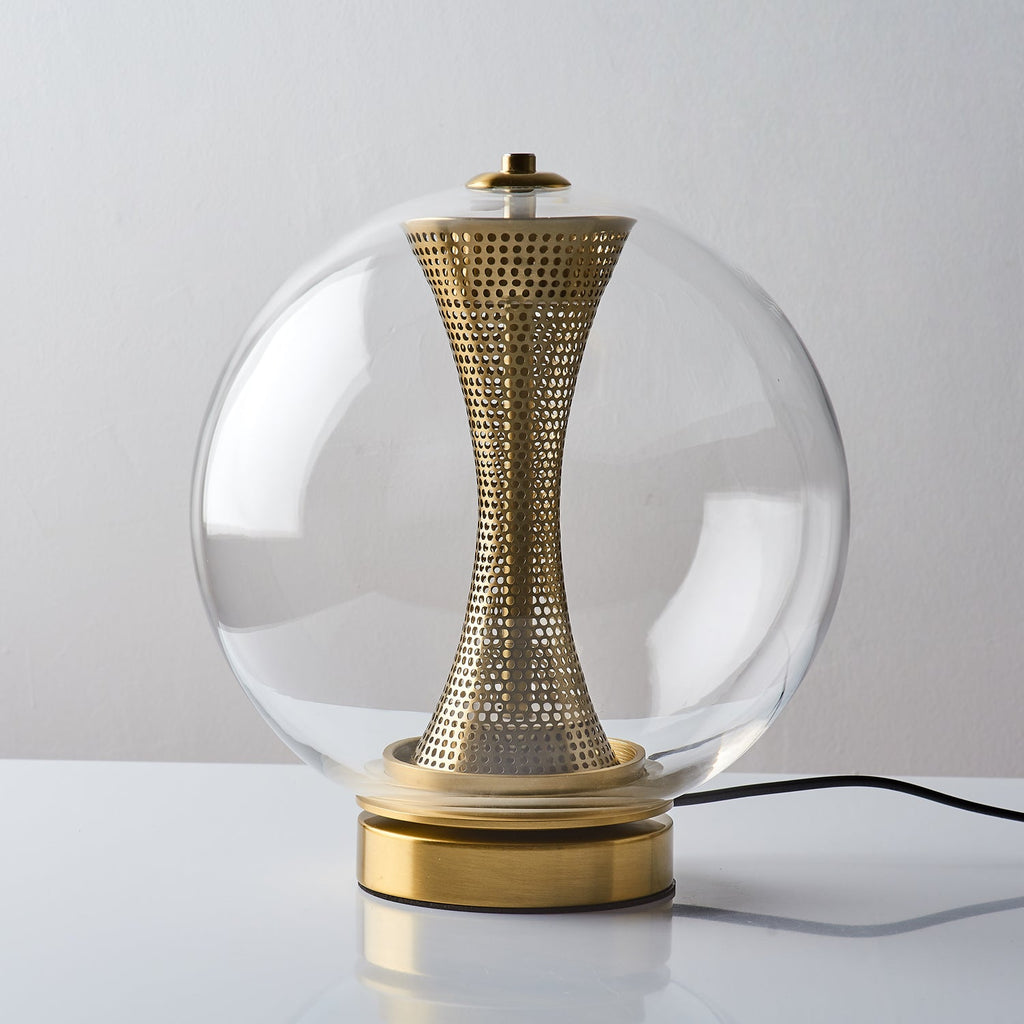 Unlit, this Clérachic clear-glass sphere lamp shows the perforated brass hourglass column, with a black cord trailing from the base.