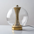 Unlit, this Clérachic clear-glass sphere lamp shows the perforated brass hourglass column, with a black cord trailing from the base.