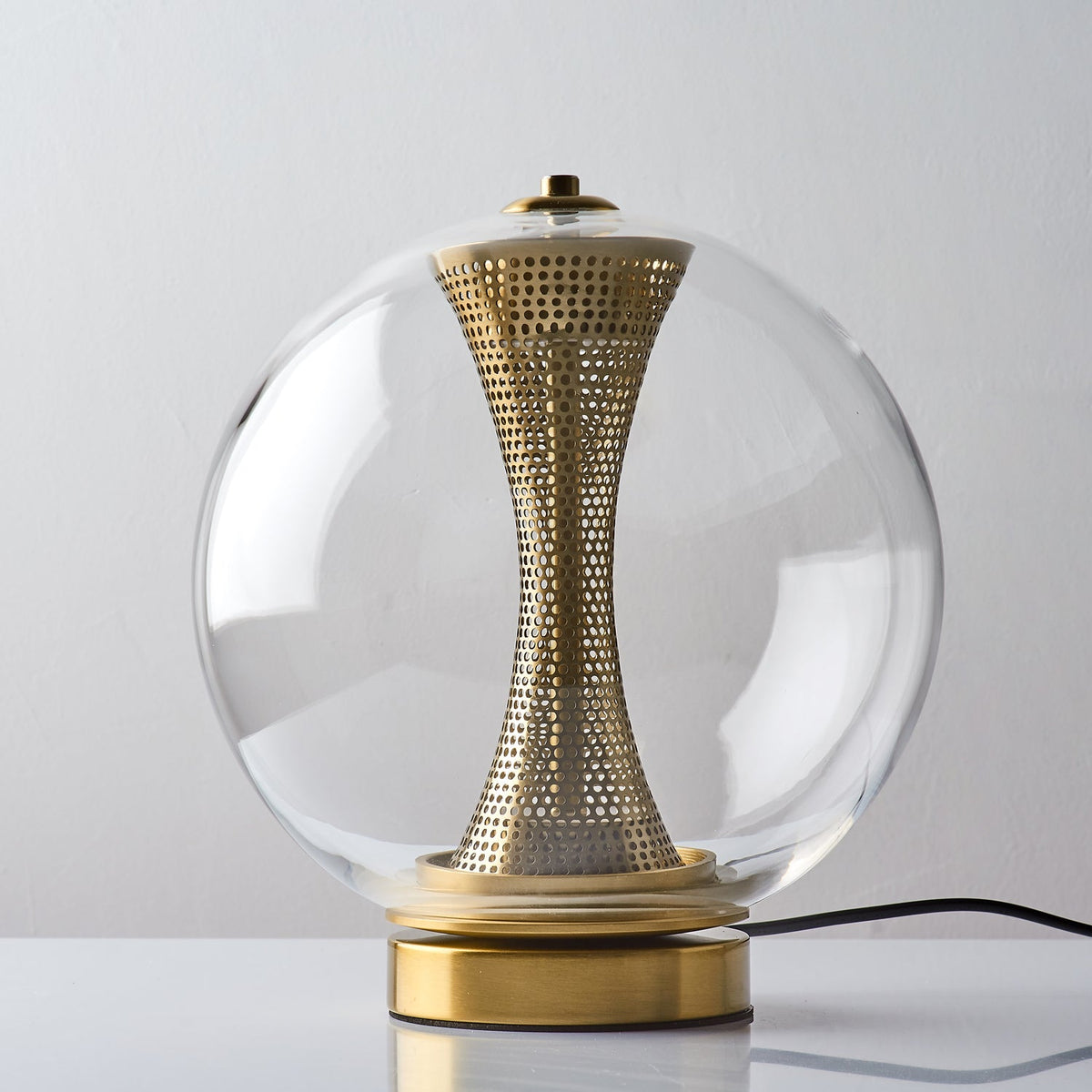 Unlit Clérachic clear-glass sphere lamp front on, the brass column pale and perforated above a brushed gold base.