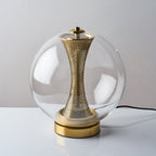 Slightly raised view of this unlit Clérachic clear-glass lamp, with its black cord and the brass column inside the sphere.