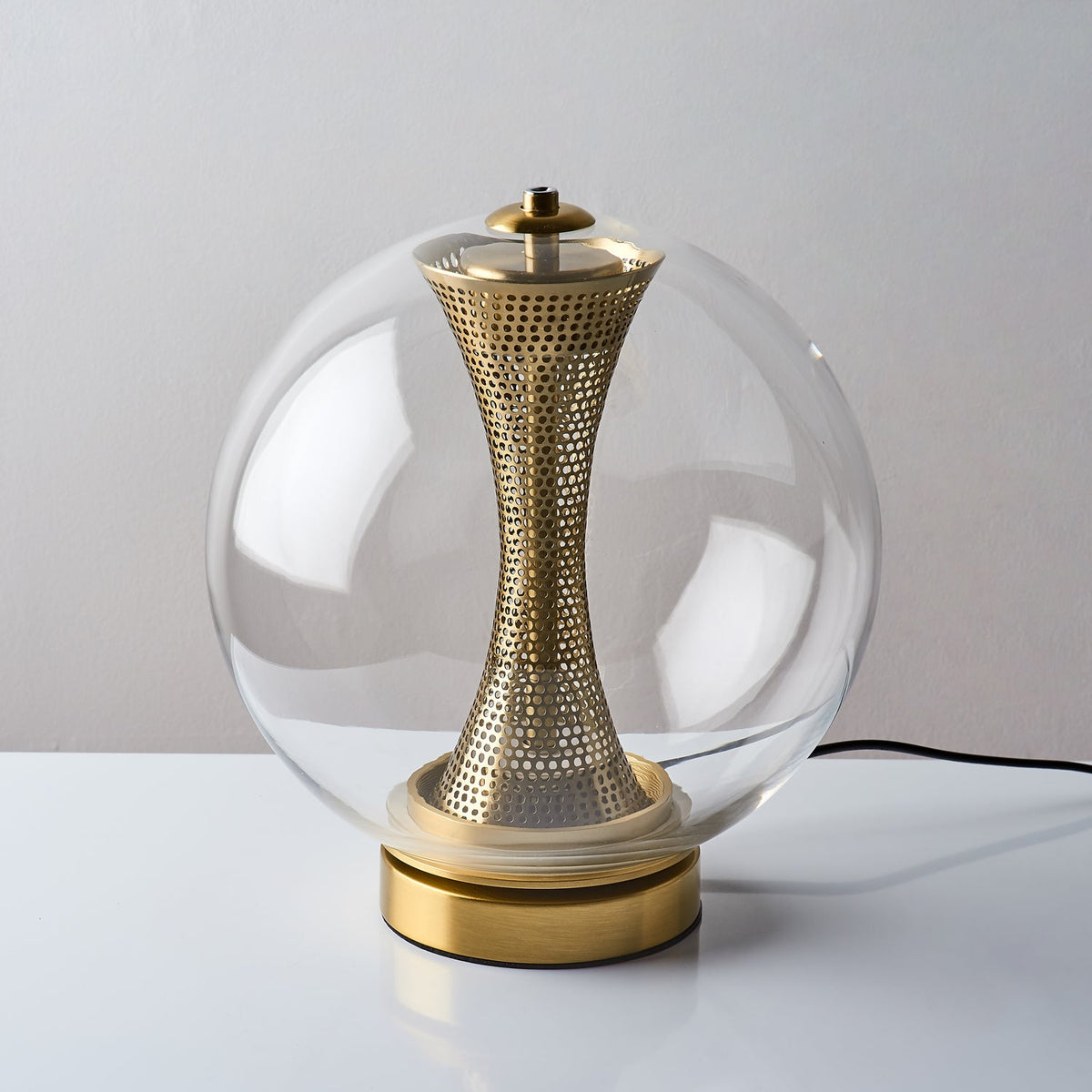 Slightly raised view of this unlit Clérachic clear-glass lamp, with its black cord and the brass column inside the sphere.