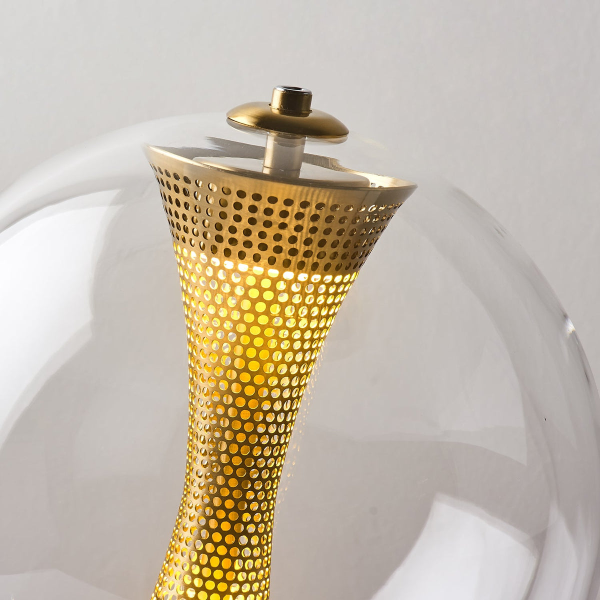 Close view of the lit perforated brass column and the small cap at the top of the glass in this Clérachic sphere lamp.