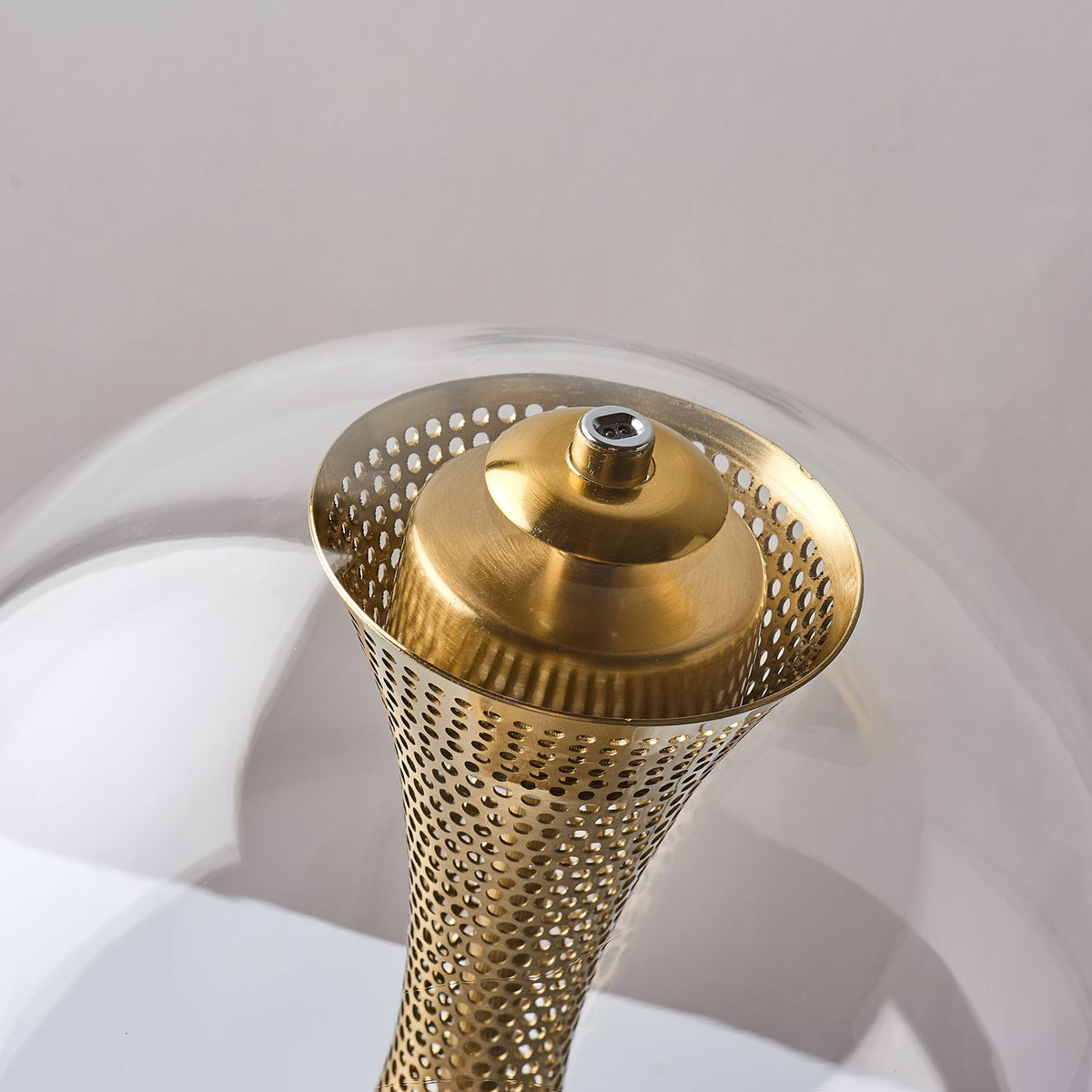 Close view of the flared, perforated top of the brass column and its cap inside the glass sphere of this Clérachic lamp.