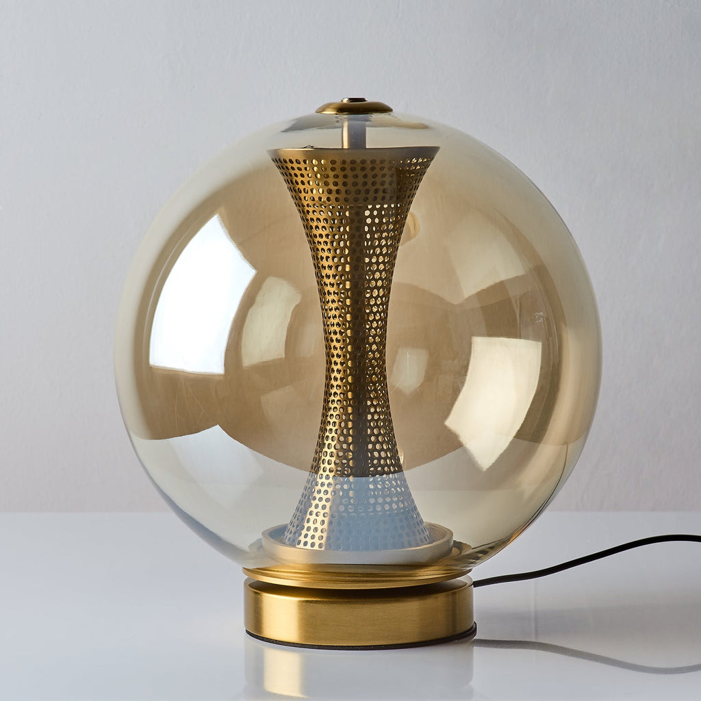 Unlit Clérachic cognac glass sphere lamp on a white surface, the tinted glass showing the perforated brass column inside.