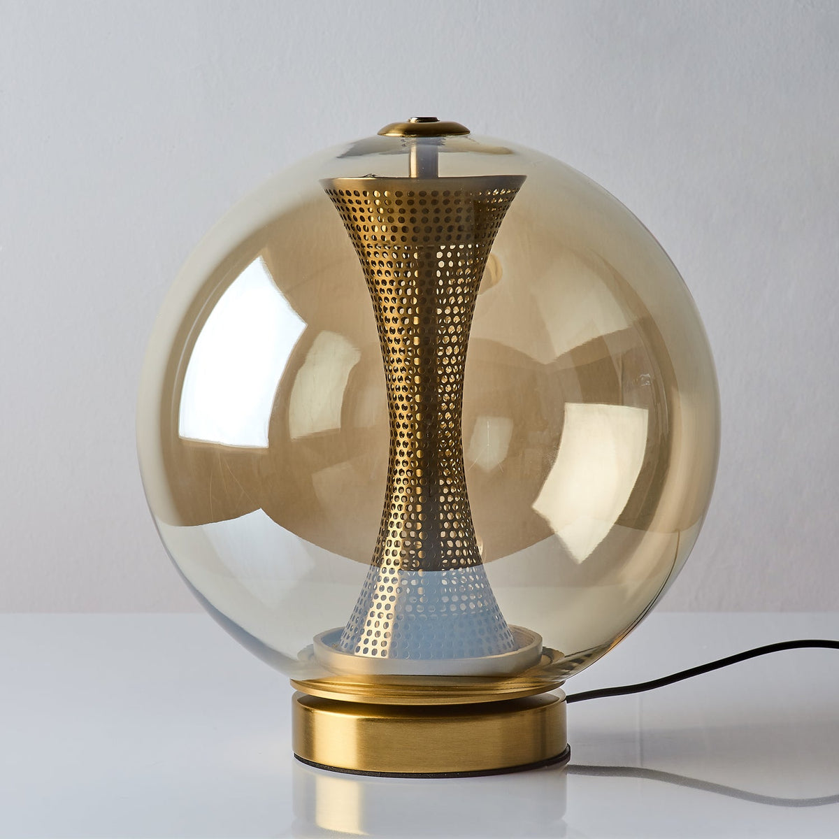 Unlit Clérachic cognac glass sphere lamp on a white surface, the tinted glass showing the perforated brass column inside.