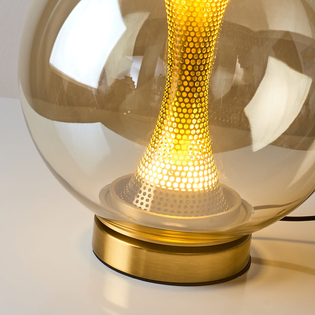 Close view of the lit lower column of this Clérachic cognac sphere lamp, with its pale collar and brushed gold base.