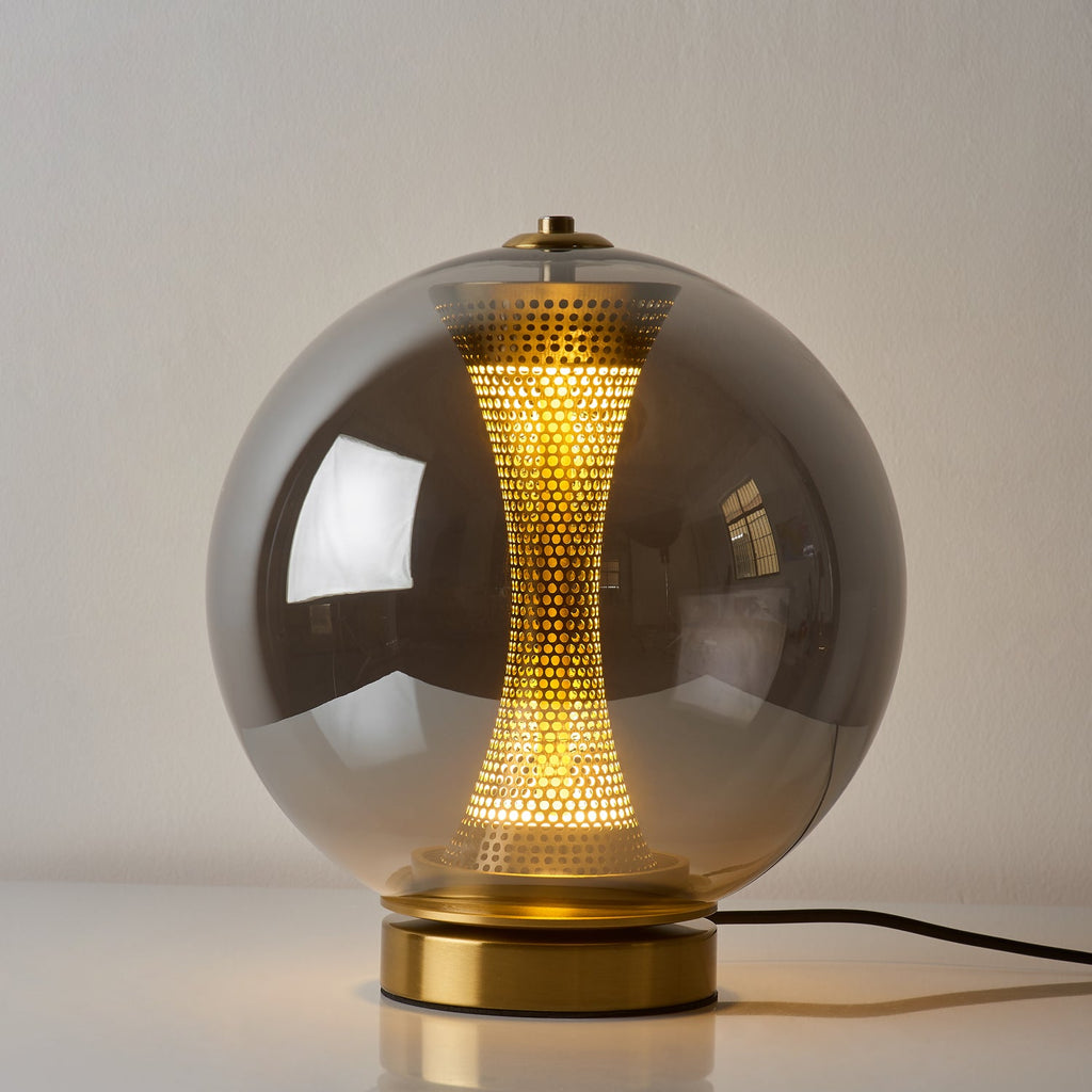This Clérachic smoky grey sphere lamp, lit, with the glow of the perforated column showing through its dark glass.