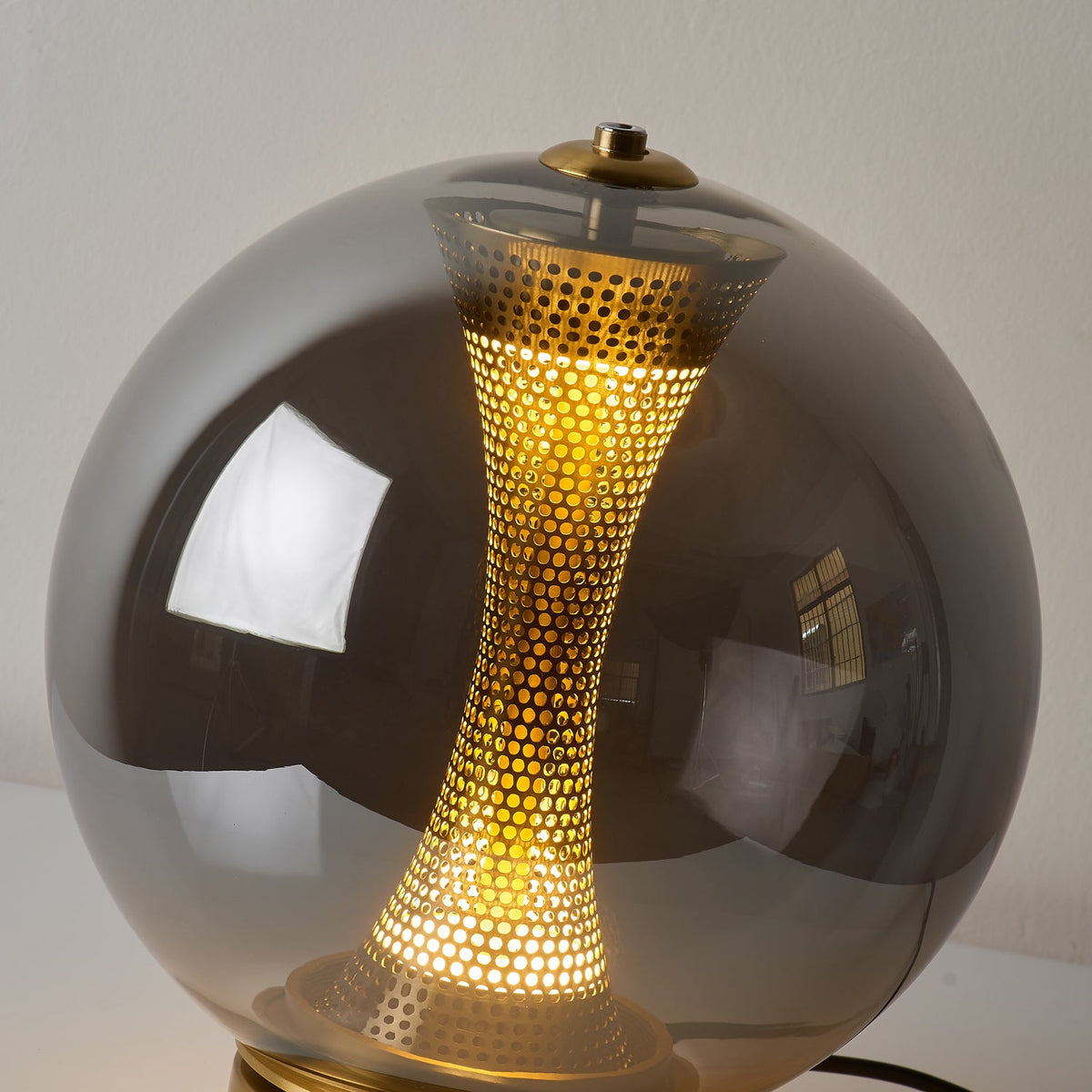 Close view of the glowing perforated brass column inside the smoky grey glass sphere of this Clérachic lamp.
