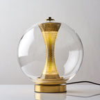 Front view of this lit Clérachic clear-glass sphere lamp, a soft glow in the perforated column above the gold base.
