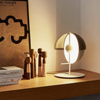 On a wooden shelf beside carved figures and books, this white-based Clérachic table lamp glows warm through its dome and half-sphere.