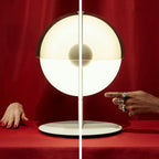 Close view of a white-based Clérachic table lamp against red fabric, with its glowing half-sphere and central ball in focus.