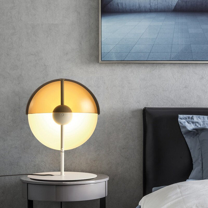 A white-based Clérachic table lamp glows warm on a round bedside table beside a dark headboard and a grey concrete wall.