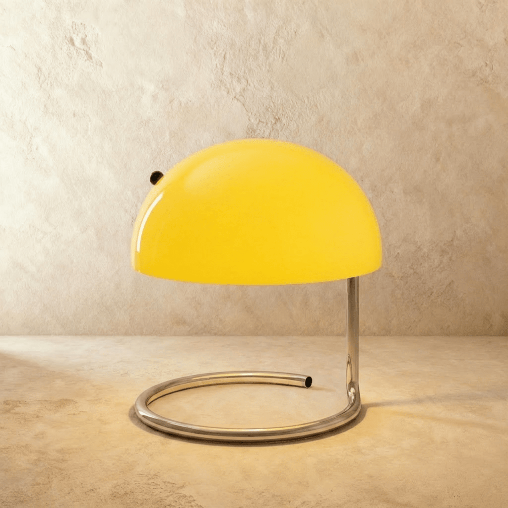 Clérachic's yellow dome table lamp glows atop a spiral chrome base against a warm plaster wall.