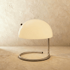 Clérachic's white dome-shade table lamp sits on its chrome spiral base against a plaster backdrop.