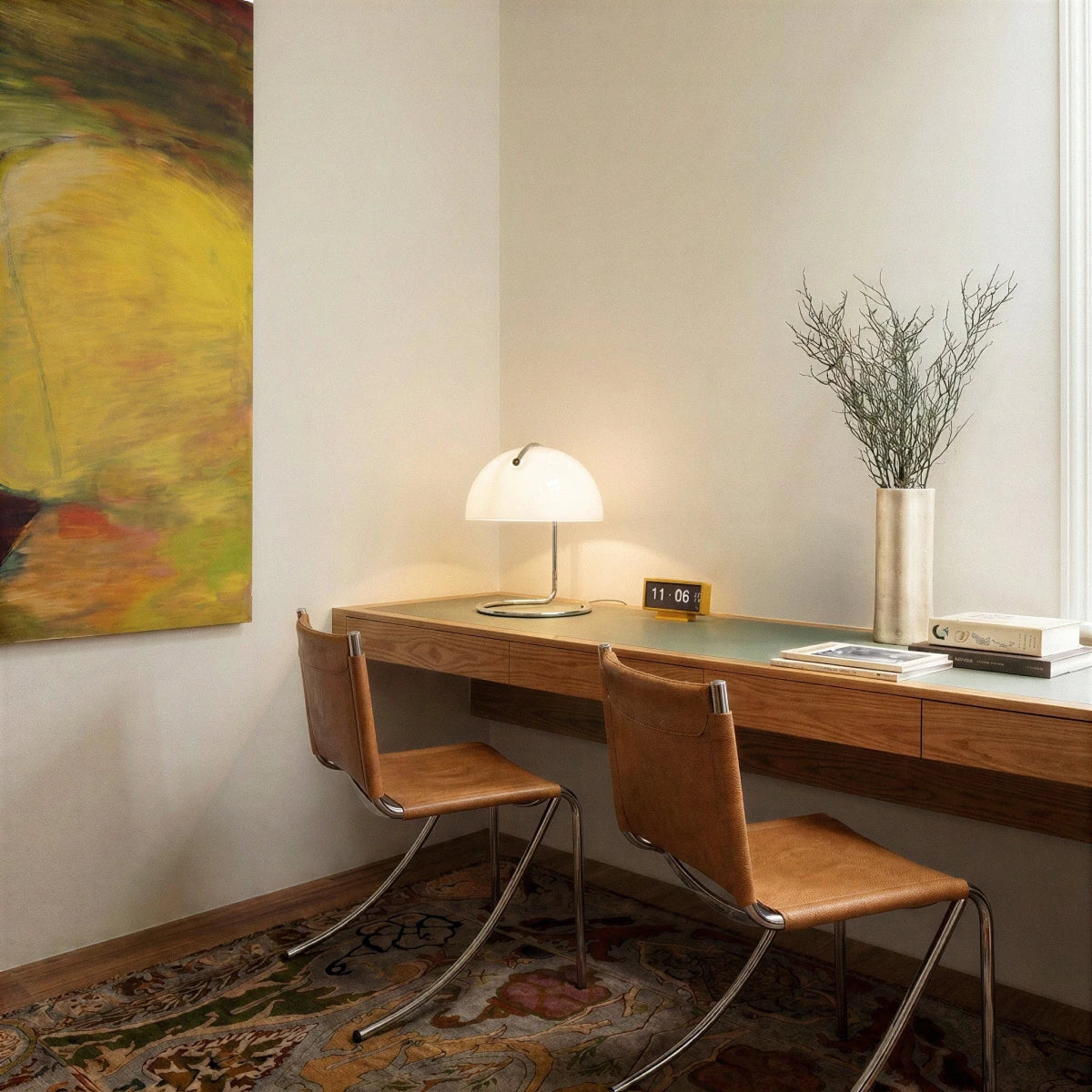 A lit Clérachic white dome lamp sits on a wooden desk beside a digital clock and dried branches.
