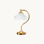 A Clérachic table lamp on a plain white backdrop, with a frosted white scalloped glass shade on a curved brass arm and a round gold base.